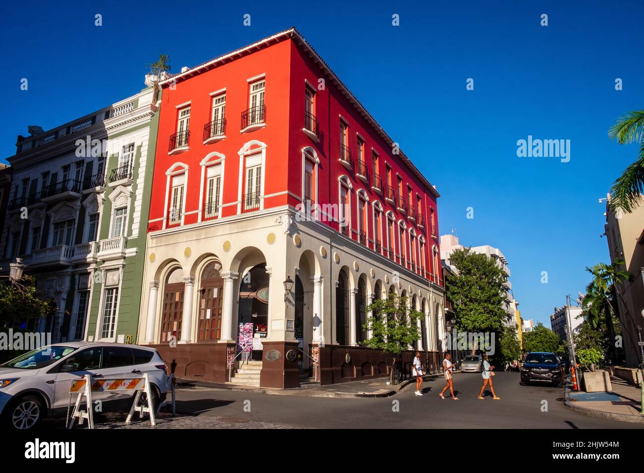 Tres mujeres cruzan la calle frente a un histórico edificio rojo en la Calle del Recito Sur, Viejo San Juan, Puerto Rico Foto de stock