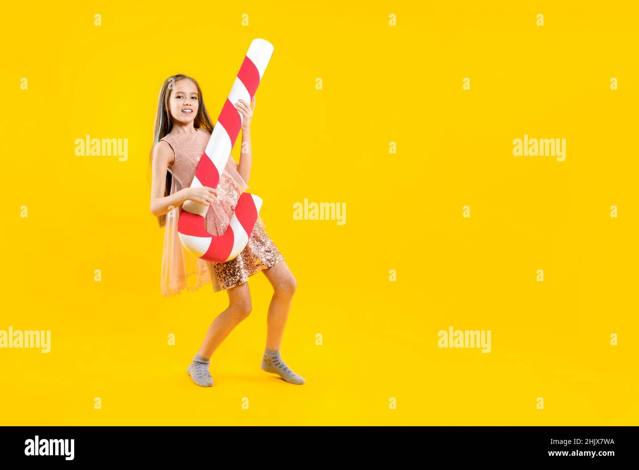 Dulces para Navidad. Una hermosa chica sostiene un enorme caramelo en sus manos, finge tocar la guitarra. Lollipop. Guitarrista. Foto de stock