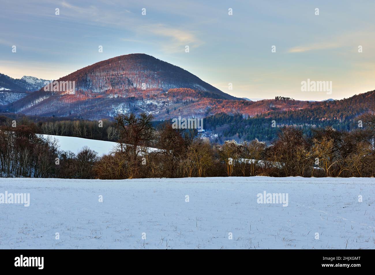 Paisaje invernal de montaña iluminado por los últimos rayos del sol poniente. Hermosas colinas y bosques. Cielo azul al atardecer. Vrsatec, Eslovaquia. Foto de stock