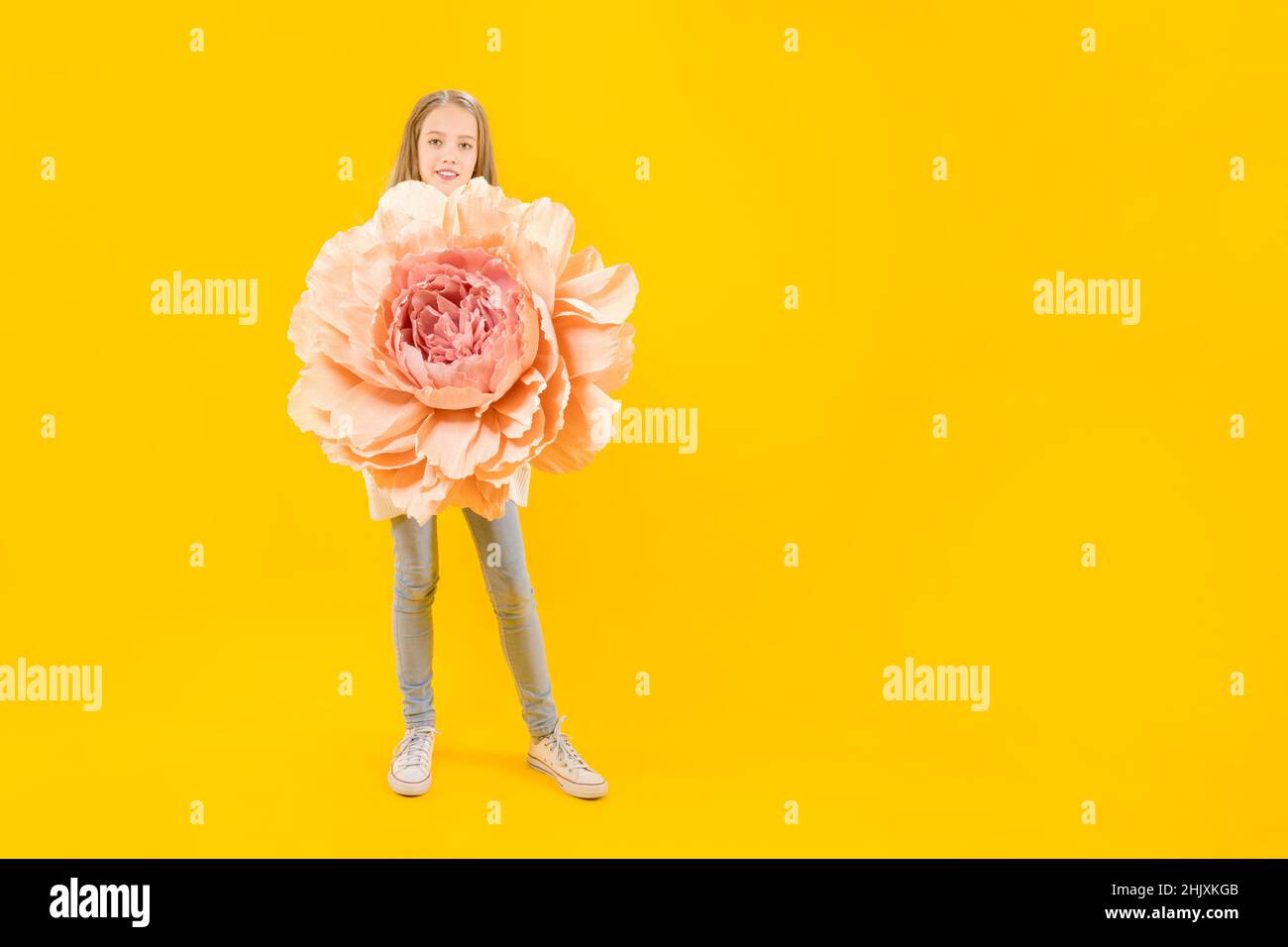 Hermoso brote. Una chica linda sosteniendo una enorme flor de peonía en sus manos sobre un fondo amarillo. Foto de stock