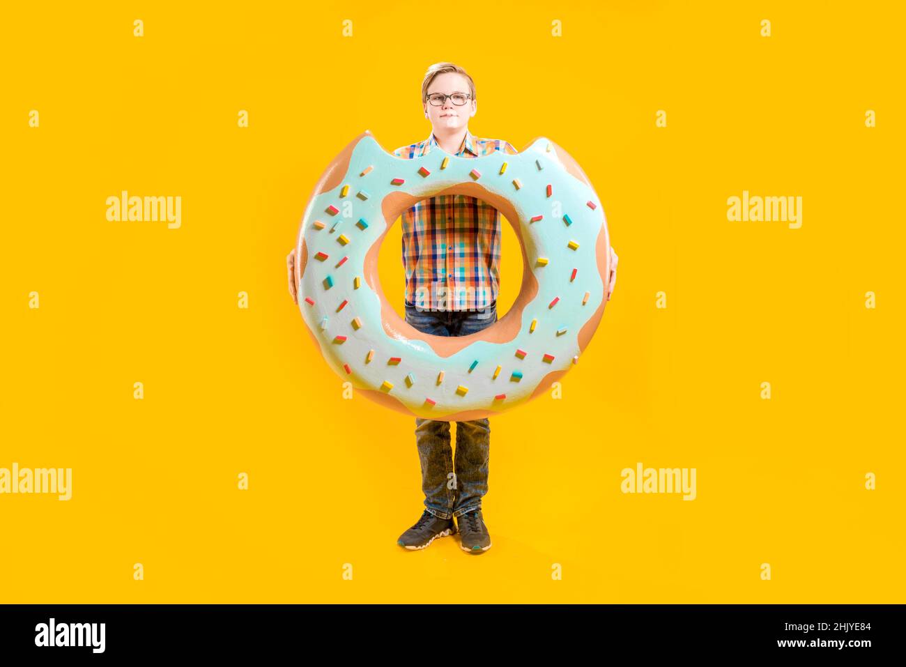 Un chico lindo está sosteniendo un enorme donut en sus manos. Adolescente alegre. Confitería. Delicioso postre. Un tipo con una cara divertida. Foto de stock