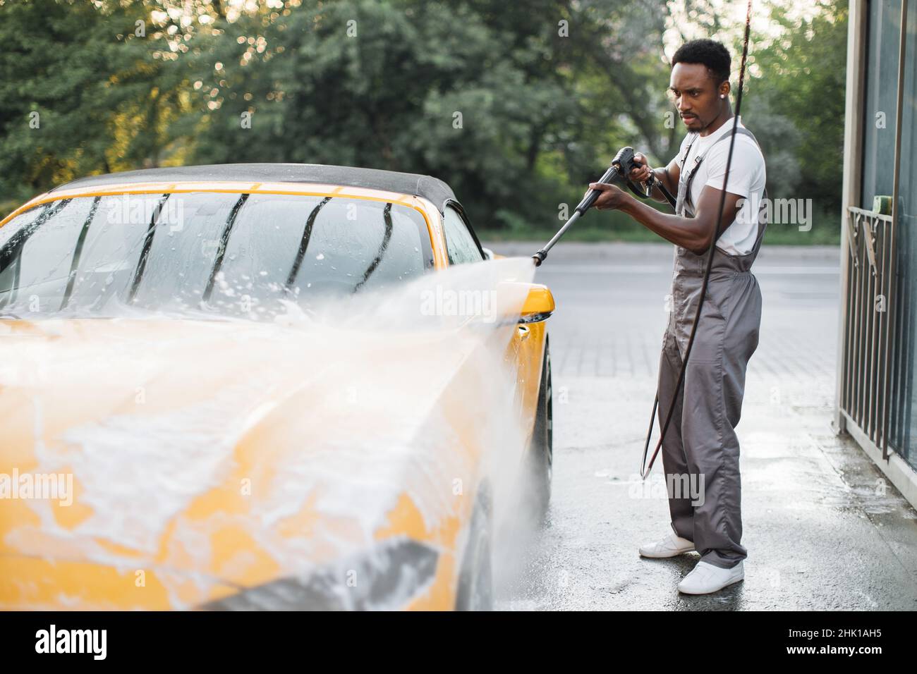Lavar el coche y limpiar con jabón y esponja. Joven trabajador africano  americano concentrado, con overoles grises y guantes negros lavando la  capucha de coche jabonosa Fotografía de stock - Alamy