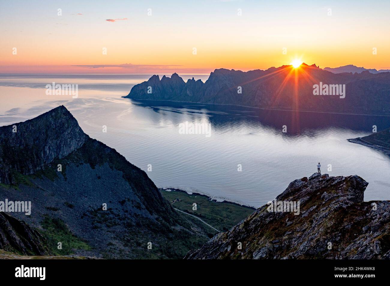 Persona admirando el fiordo al amanecer sobre la montaña Husfjellet, isla Senja, condado de Troms, Noruega, Escandinavia, Europa Foto de stock