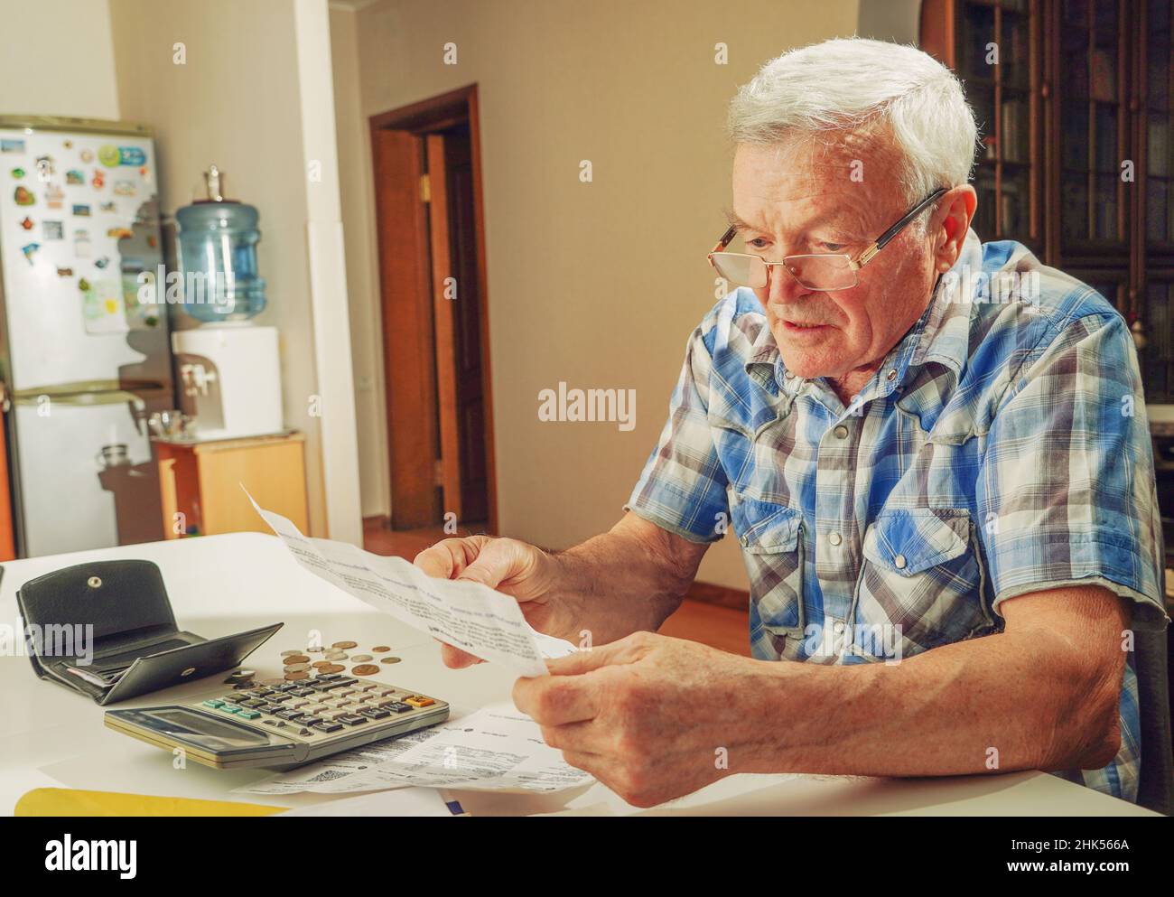 Hombre mayor sentado en la mesa y calculando las finanzas. Hombre viejo que comprueba las cuentas. Hombre contando monedas en la mesa. Concepto de cálculo de pensiones Foto de stock