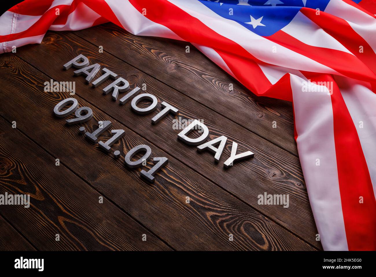 las palabras patriota día puso con letras de metal plateado en la superficie de la tabla de madera con la bandera ee.uu. arrugada Foto de stock