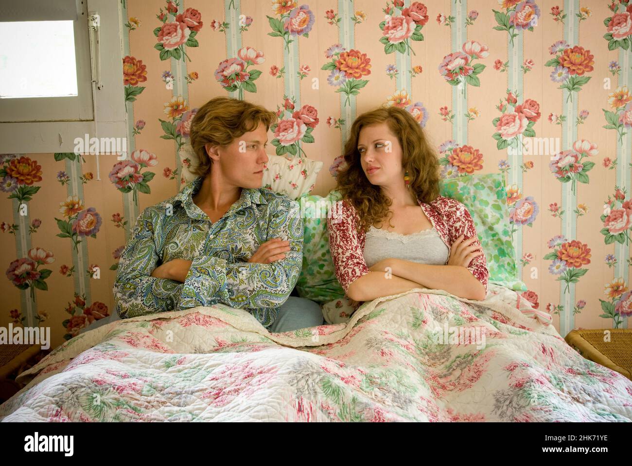 Una pareja joven tumbada en la cama mirando uno al otro en el dormitorio con paredes de papel pintado floral Foto de stock