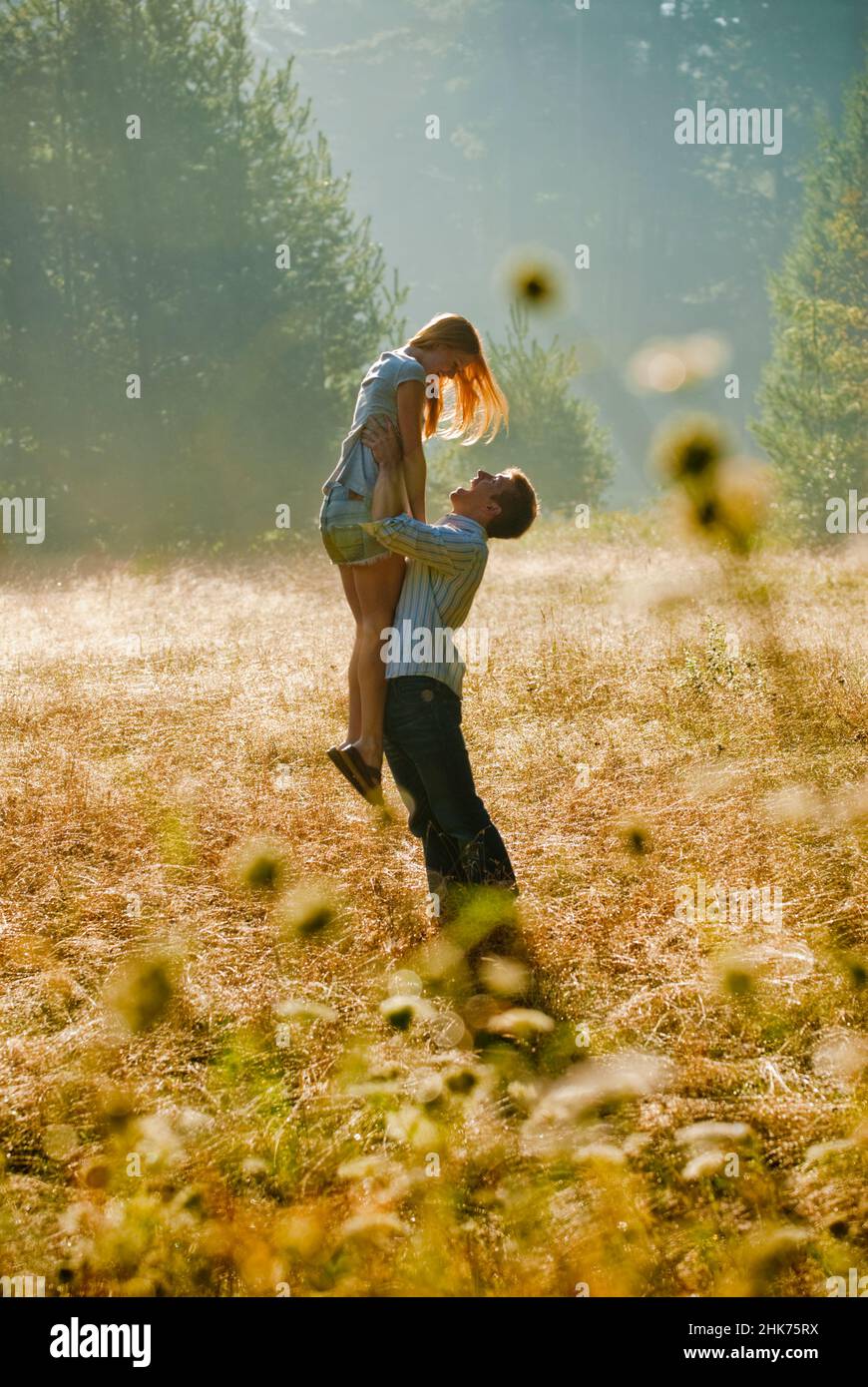 Joven pareja en un campo brillante, el hombre sosteniendo a la mujer en alto Foto de stock