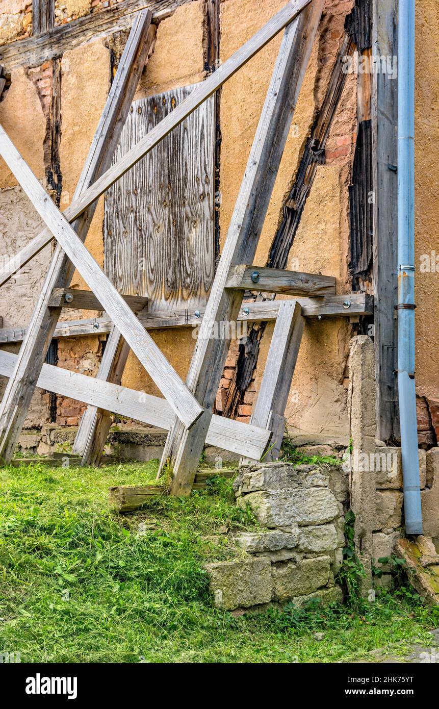 Una antigua casa de entramado de madera está sostenida por una estructura de apoyo. Foto de stock