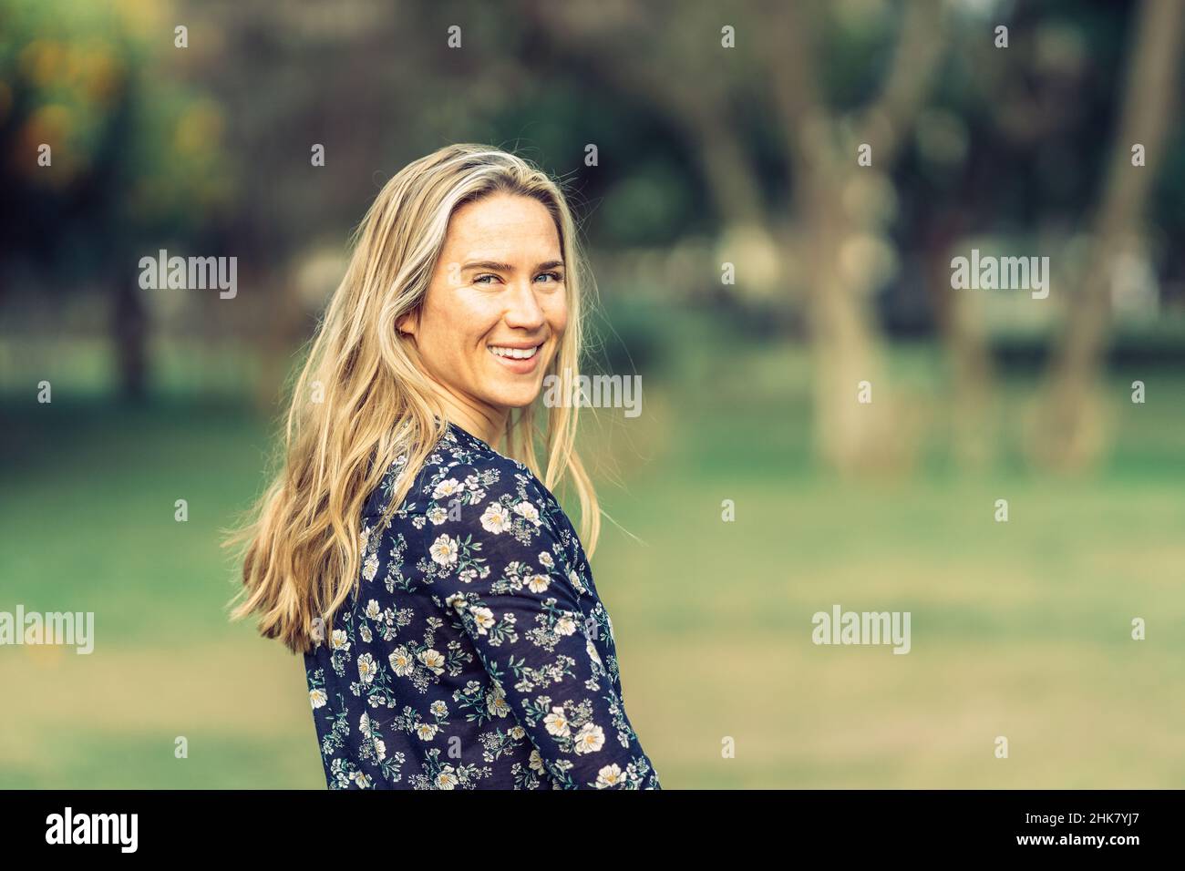 mujer en sus treinta vueltas sonriendo a la cámara en una camisa florida Foto de stock