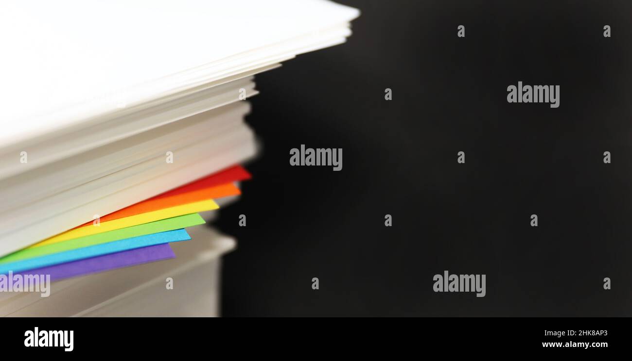 gay lesbiana bisexual queer transgender comunidad arcoiris bandera colores poking fuera de una resma de papel blanco crujiente de la oficina sobre un fondo negro liso. Foto de stock