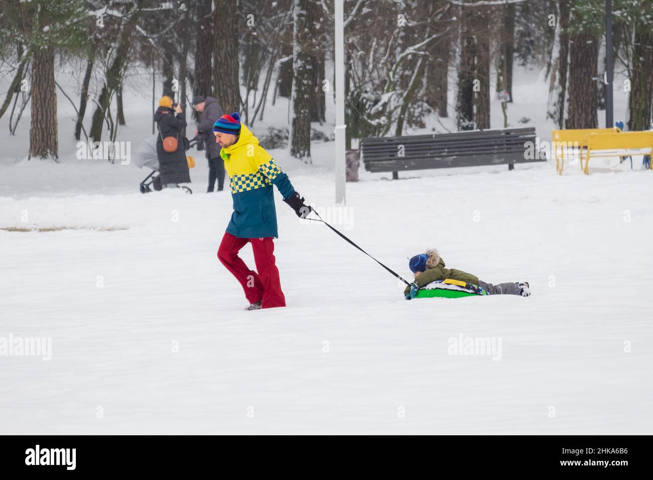 Padre triste tira de un trineo (tubing) en la nieve en el parque, y su hijo miente en el trineo y disfruta de la diversión en invierno. Foto de stock