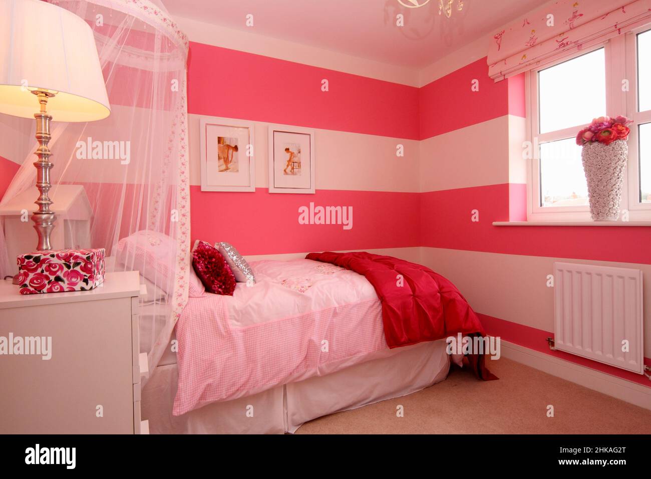 Dormitorio de chicas rosa y blanco, coronilla con dosel, fotos bailarinas de ballet en la pared, luz al lado de la cama. Foto de stock