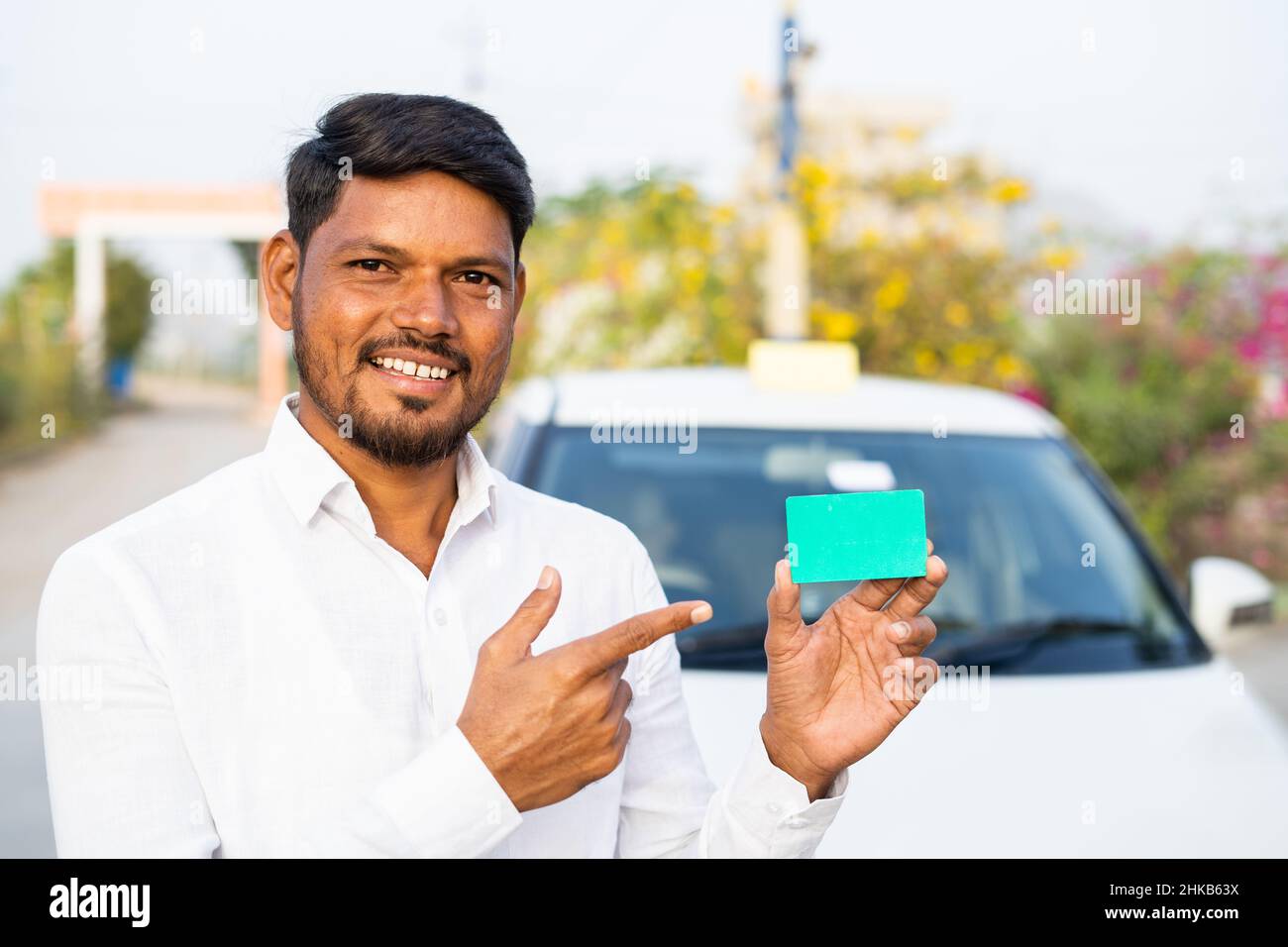 sonriente conductor de taxi mostrando una tarjeta vacía mirando la cámara delante del coche - concepto de tarjeta de identificación de empoyee, publicidad y promociones. Foto de stock