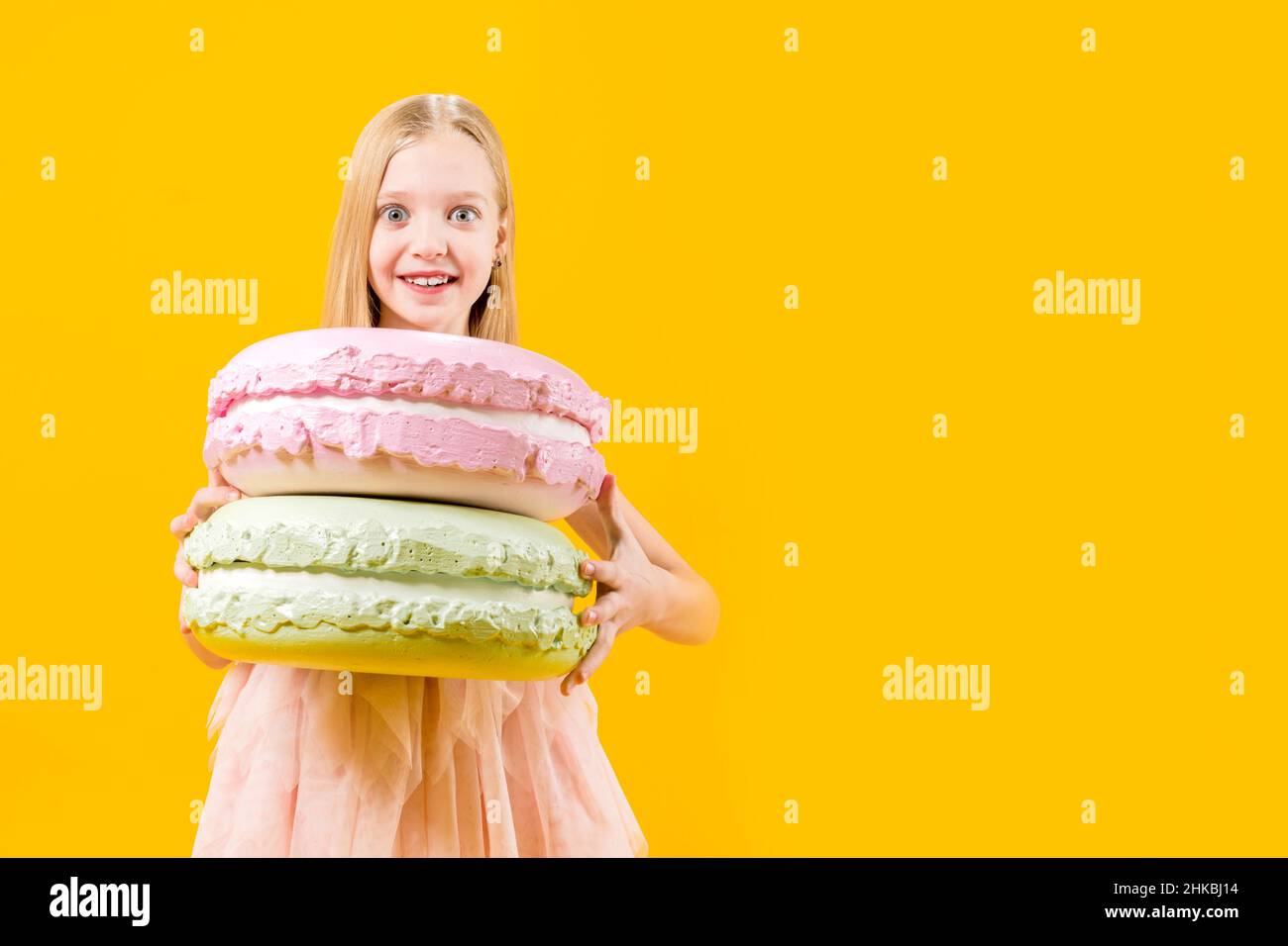 Regalo dulce. Una chica linda está sosteniendo dos enormes macaroons sobre un fondo amarillo. Postre redondo. Dulzura de Navidad. Foto de stock