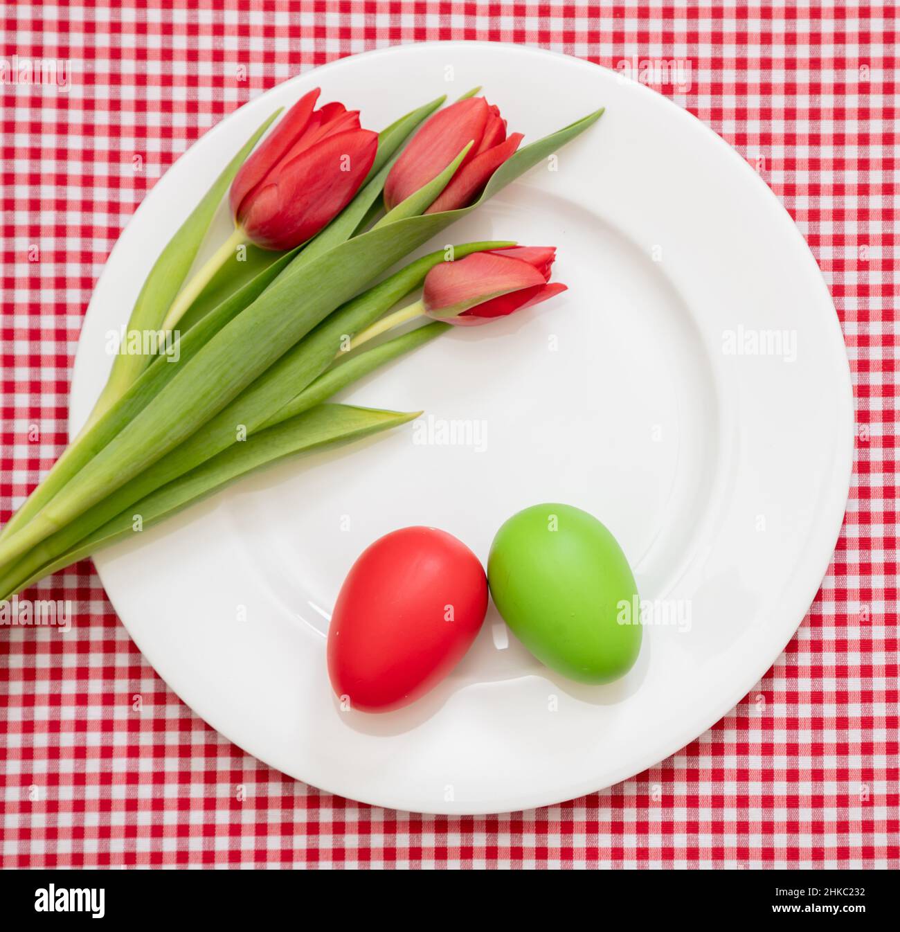 Mesa de Vacaciones de Pascua. Huevo rojo y verde y la decoración de tulipanes en plato blanco, manteles de cuadros de fondo, vista de arriba, Foto de stock