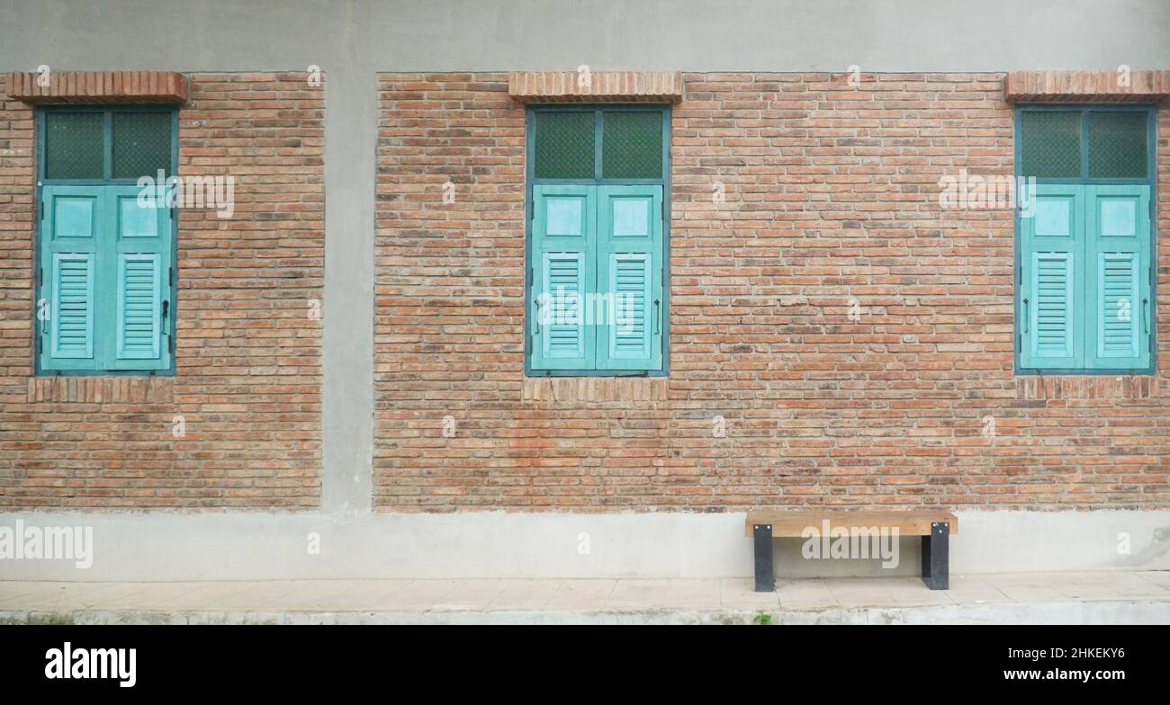 Edificio de ladrillo con ventanas y banco con cierre de madera azul Foto de stock