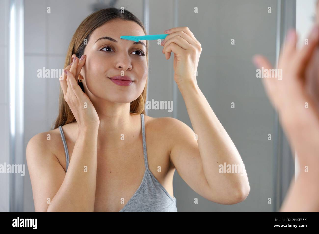 Eliminación facial del vello. Hermosa mujer joven afeitando su cara con la  navaja en casa. Una mujer bonita usando la afeitadora en el baño Fotografía  de stock - Alamy