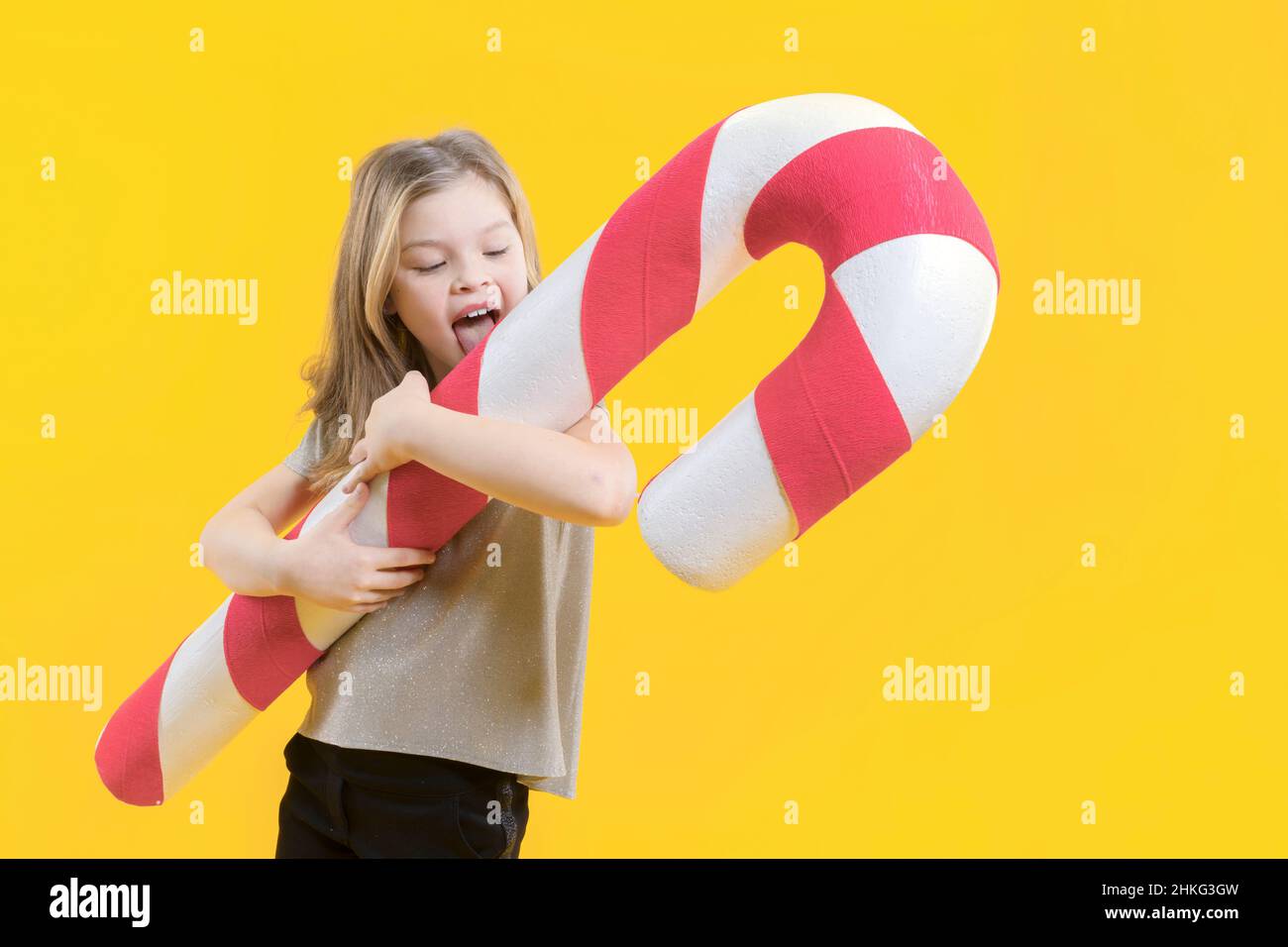 Una chica adolescente linda con deleites sosteniendo un enorme caramelo y tratando de lamer sobre un fondo amarillo. Dulces de Navidad. Feliz preescolar con dulces adentro Foto de stock