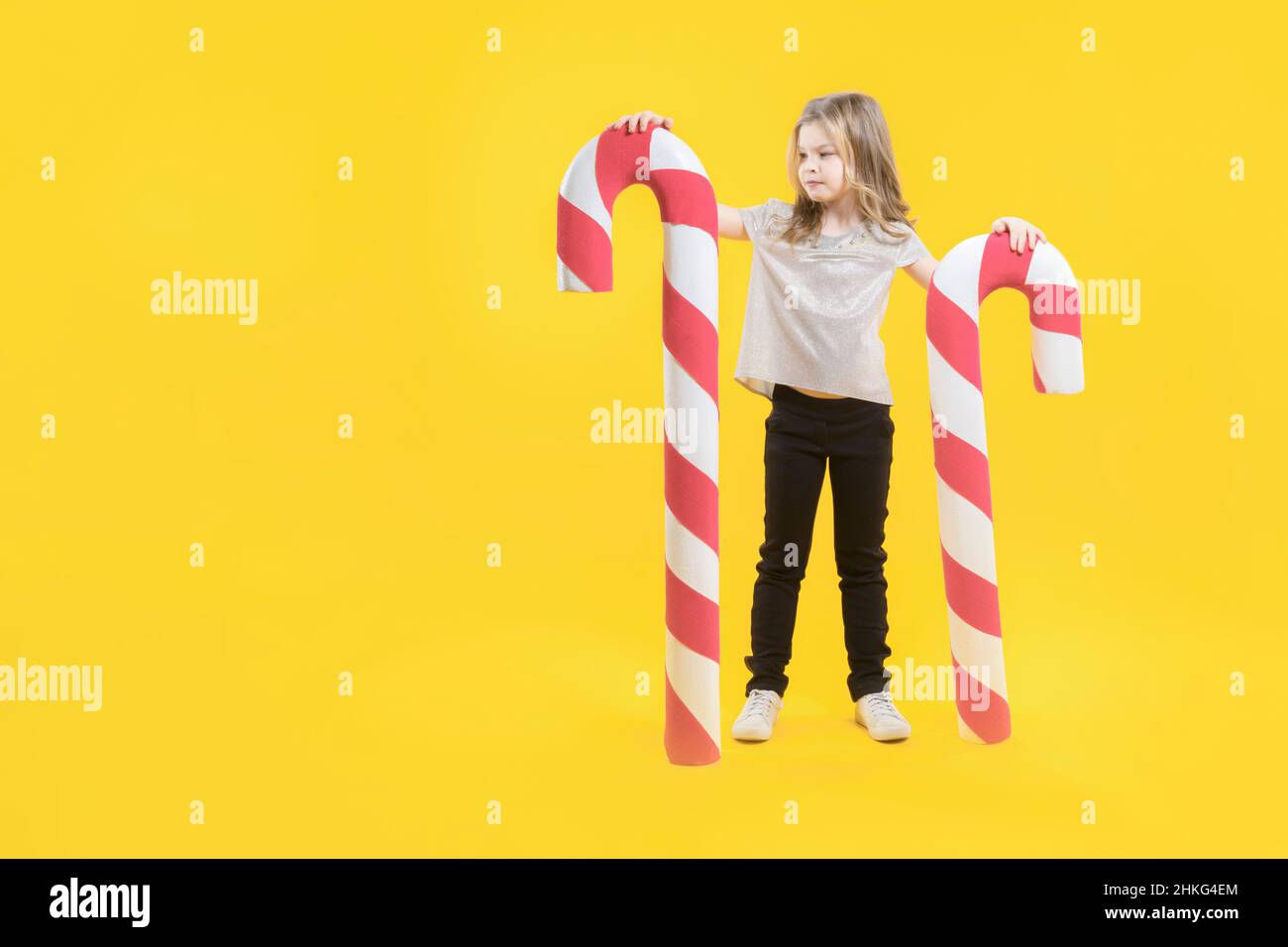 Una linda adolescente sosteniendo dos enormes dulces sobre un fondo amarillo. Feliz preescolar con dulces en las manos. Lollipop. Dulces de Navidad. Espacio de copia Foto de stock