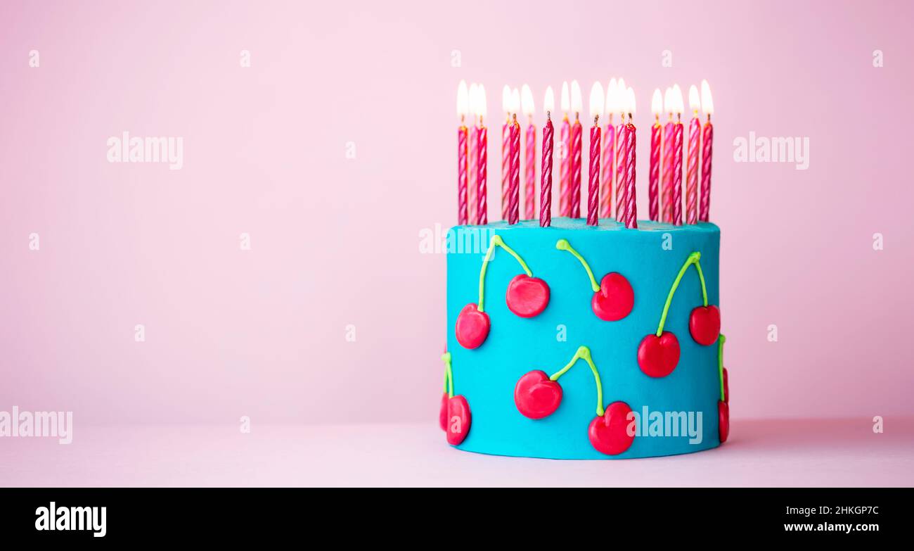 Pastel de cumpleaños de color rosa y azul decorado con cerezas de crema de mantequilla y velas de cumpleaños de color rosa Foto de stock