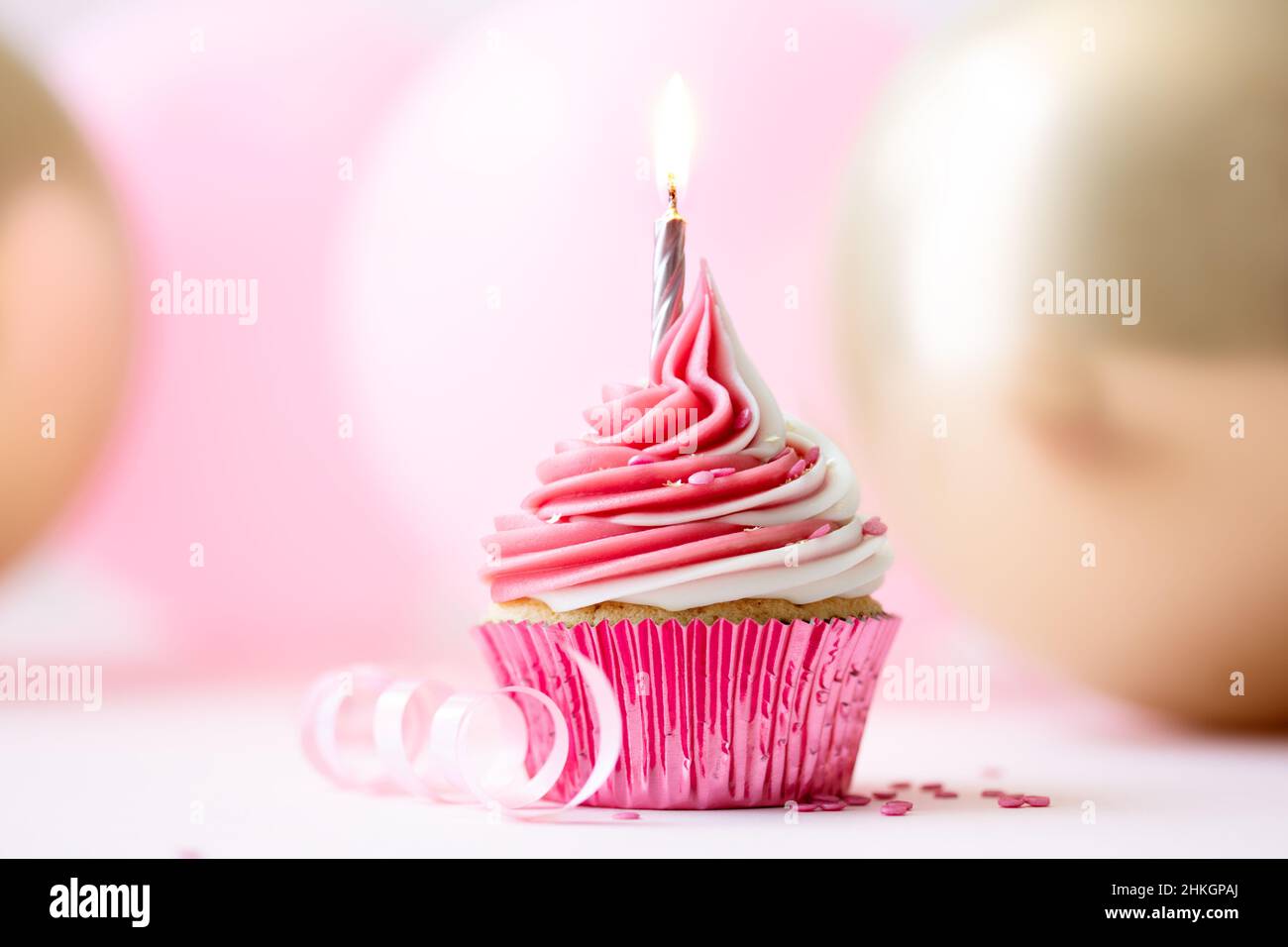 Tarta de cumpleaños rosa con una vela dorada sobre un fondo de globos rosa y dorado Foto de stock