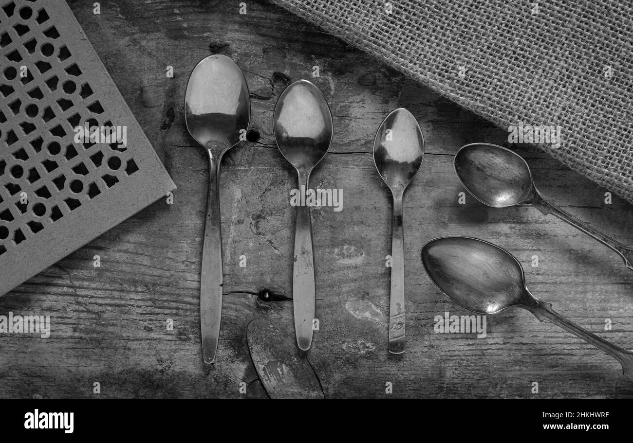primer plano macro colección de cucharas de plata vintage sobre un fondo rústico desde arriba fotografiado en blanco y negro Foto de stock