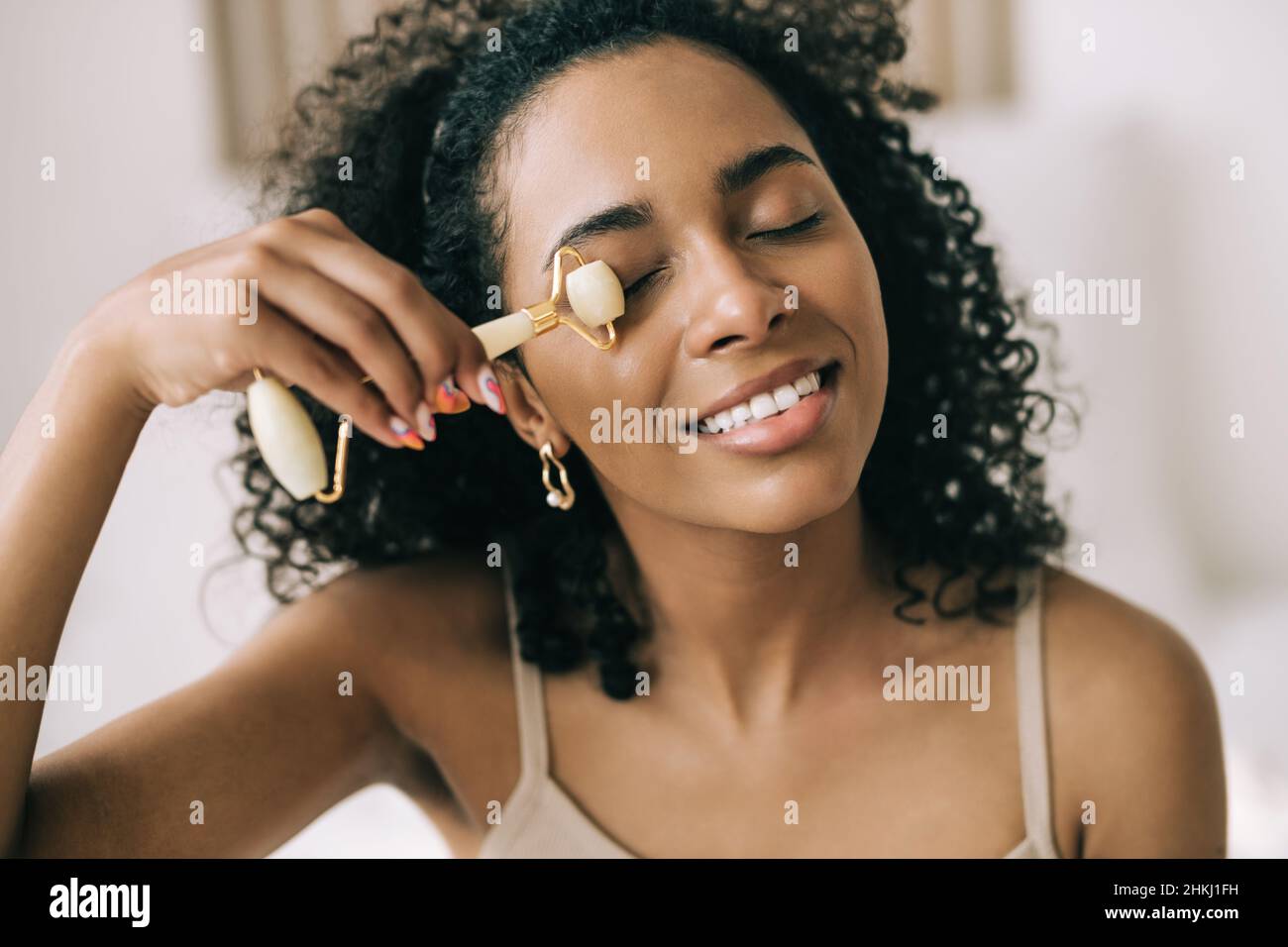 Primer plano joven mujer negra con jade piedra rodillo facial y sonrisa