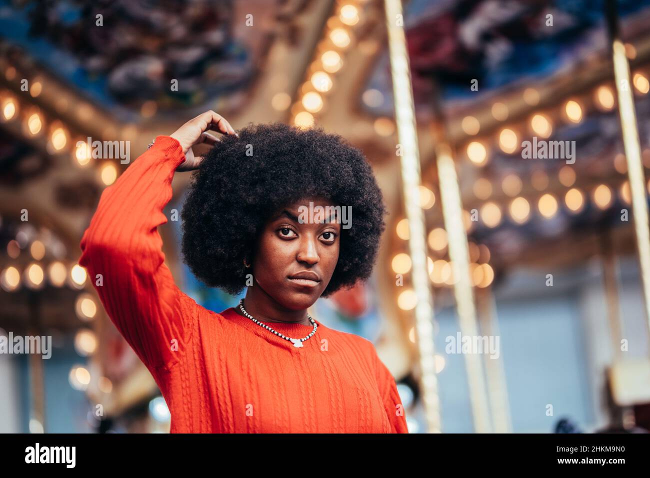 Pensive joven mujer negra con afro peinado al lado de un carrusel rascándose la cabeza. Concepto de decisión difícil Foto de stock