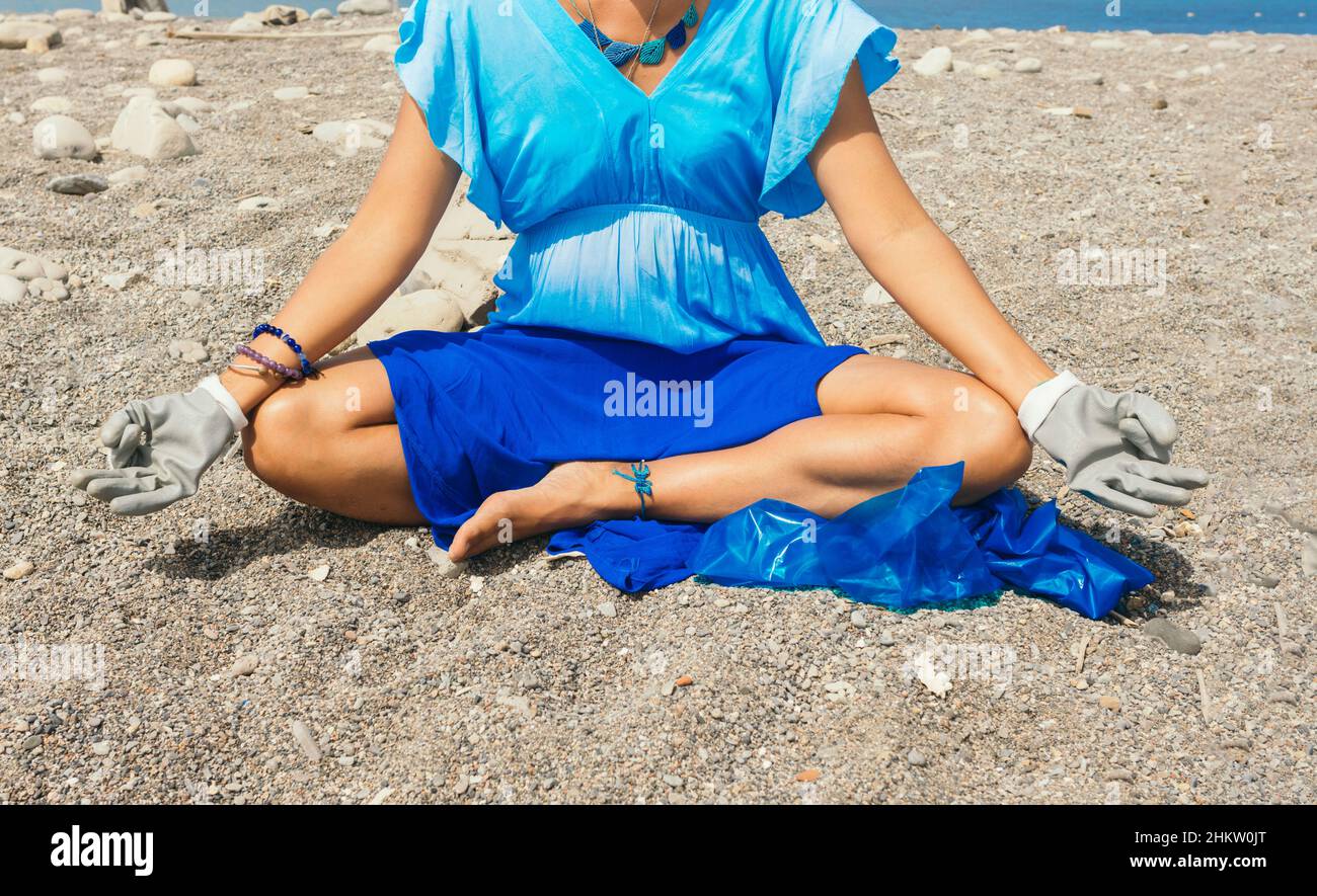 Inreconocible activista latina medita con guantes y bolsa de basura antes de limpiar una playa contaminada. Concepto de cuidado ambiental. Foto de stock