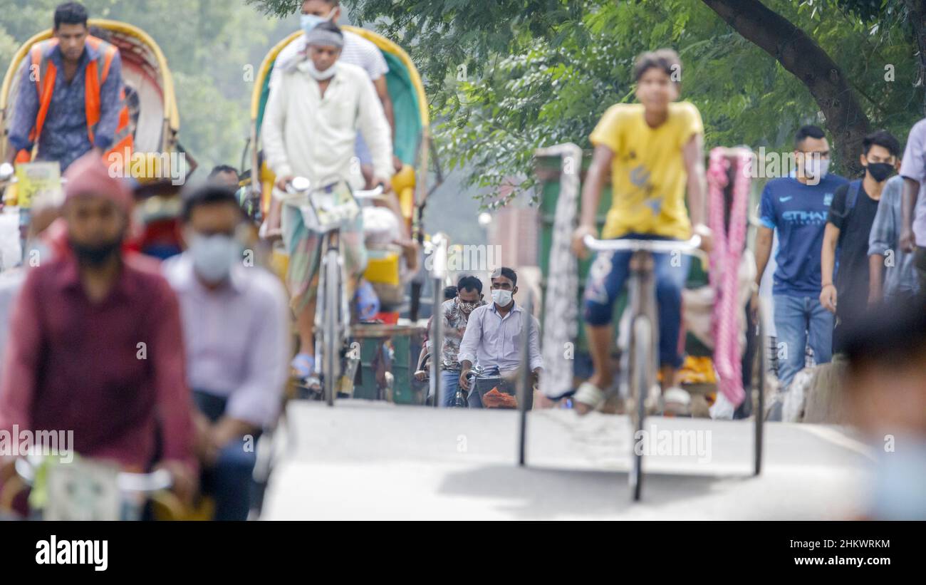 La gente caminando o montando rickshaws en su camino al trabajo en la fiebre de la mañana en Dhaka el martes 12th de julio. Bangladesh está atravesando una oleada de COVID-19, con un récord de 13768 casos el lunes 12th de julio. El 14th de julio, las restricciones de encierro se aliviarán durante nueve días para las celebraciones de Eid-ul-Azha. Foto de stock