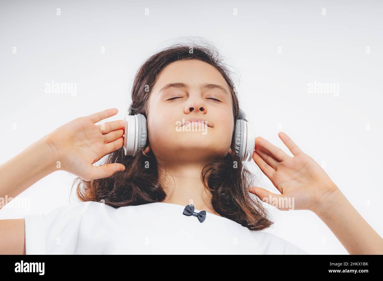 Foto de joven feliz hermosa adolescente caucásica escuchar música en los auriculares sobre un fondo de color blanco. Foto de stock para adolescentes. Hermoso brunet Foto de stock