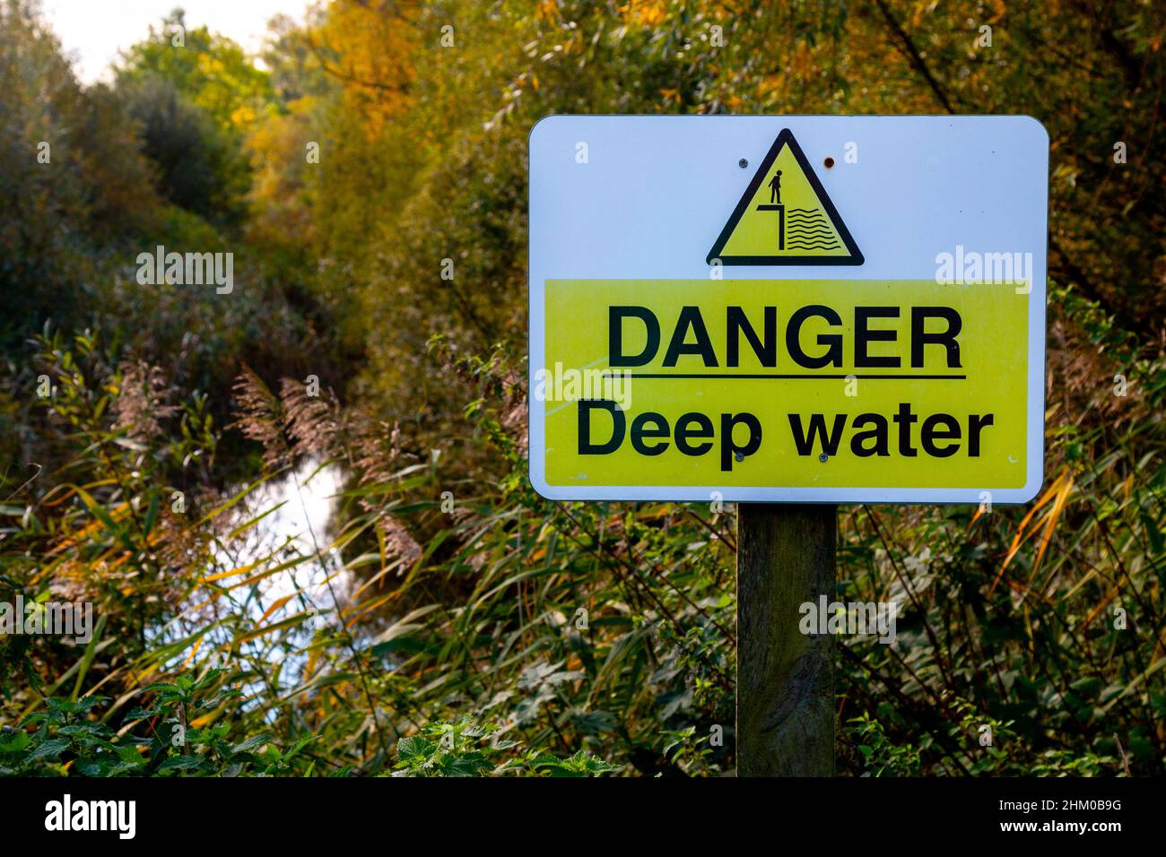 Un signo amarillo de agua profunda de peligro cerca de un estanque sobrecrecido. Trumpington, Cambridge, Reino Unido Foto de stock