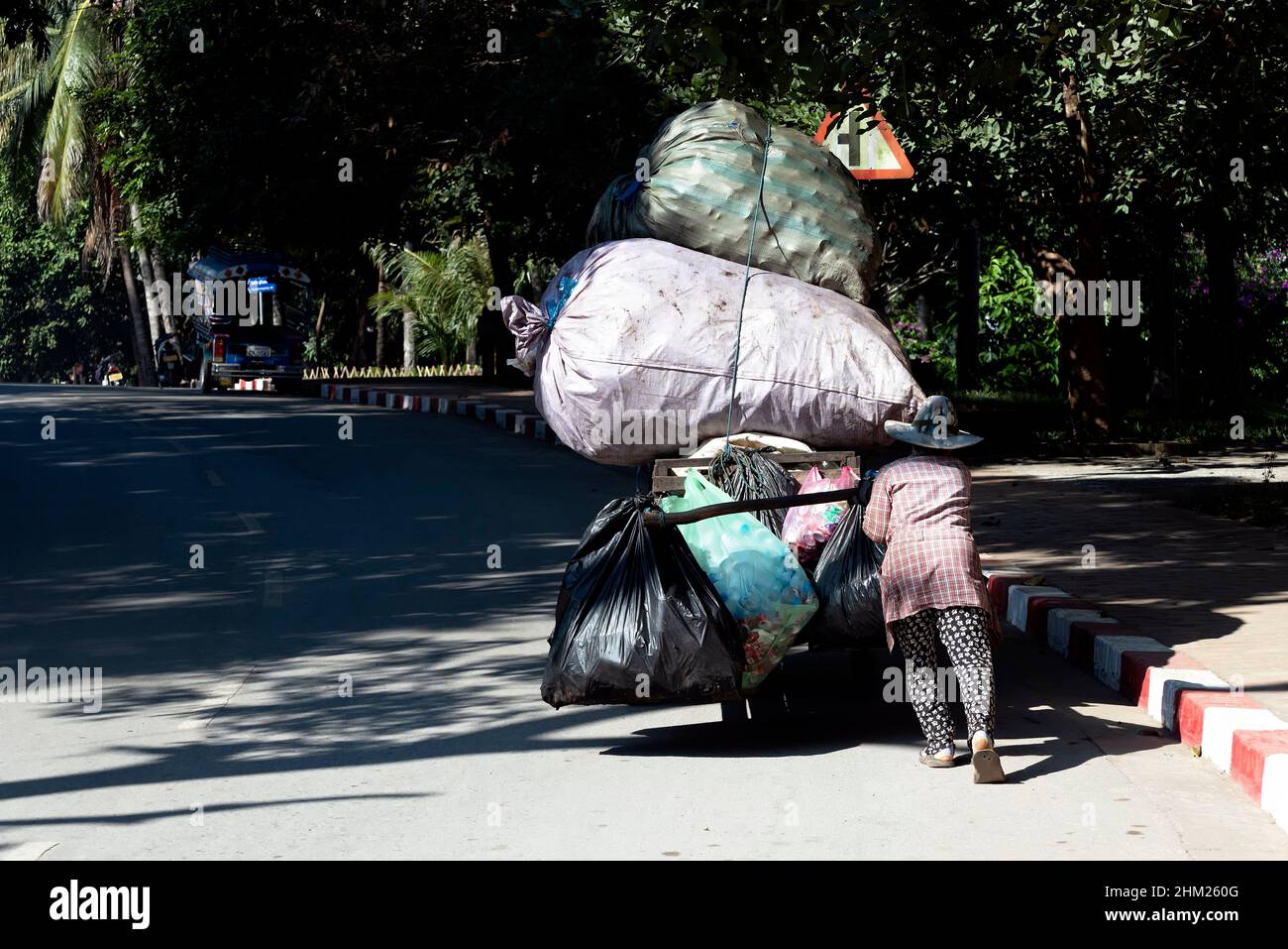 Mujer empujando un carro cargado de desechos reciclables en Luang Prabang, Laos Foto de stock
