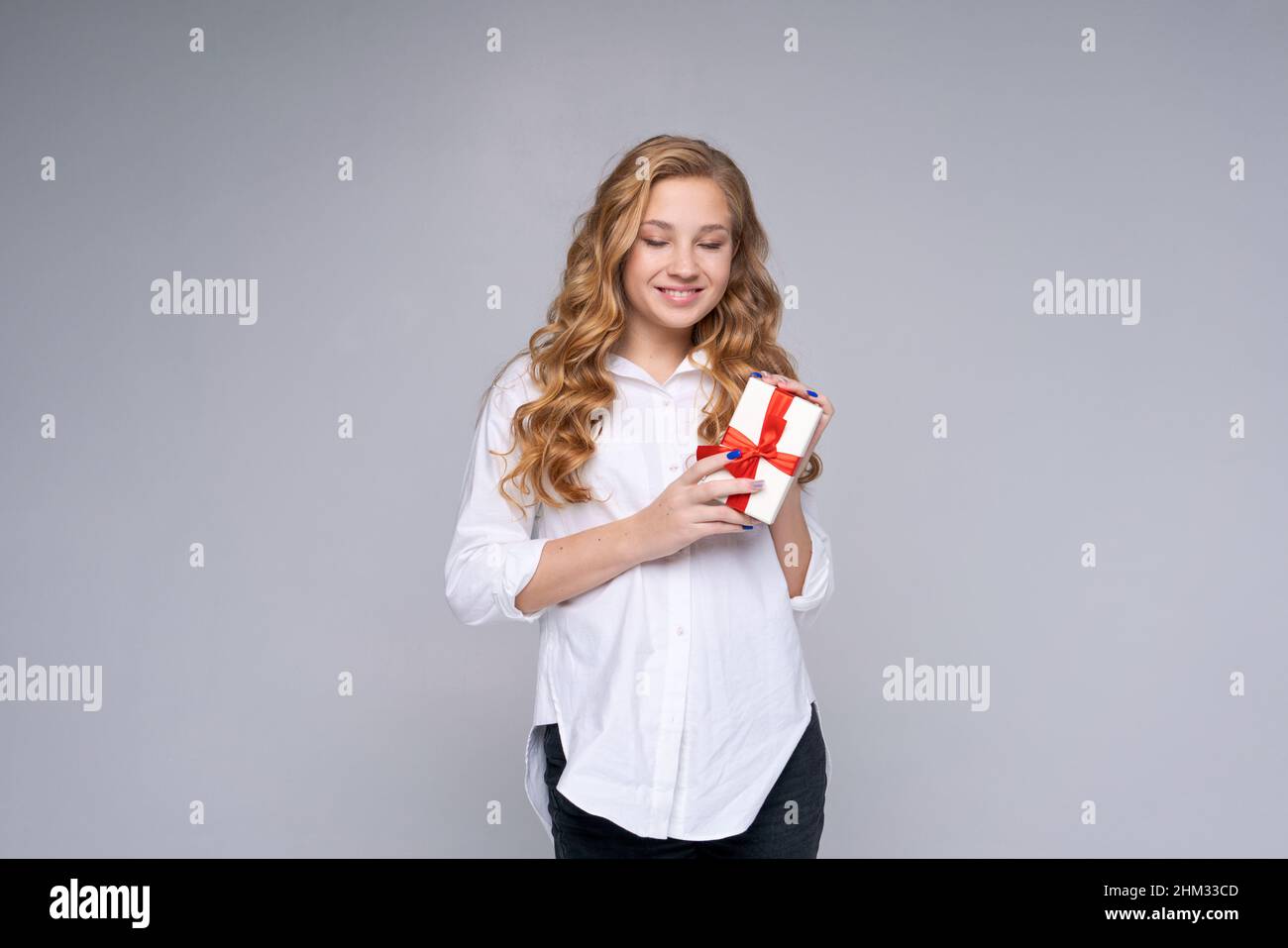 Foto alegre chica positiva sostener regalo ropa camisa blanca jeans negro,  largo pelo ondulado. Fondo de color gris claro aislado. Adolescente  caucásica feliz con un regalo Fotografía de stock - Alamy