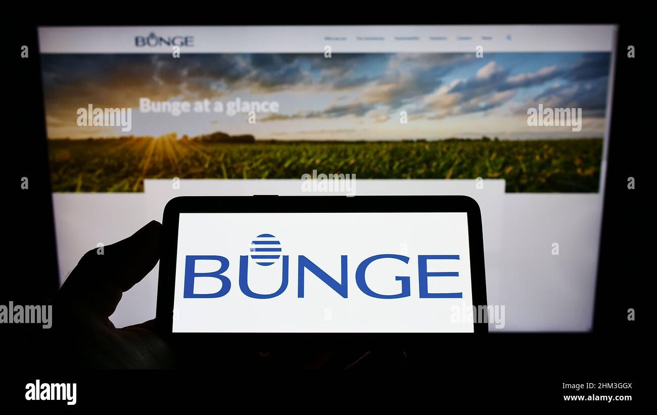 Persona sosteniendo un smartphone con el logotipo de la empresa agroindustrial y alimentaria Bunge Limited en la pantalla frente al sitio web. Enfoque en la pantalla del teléfono. Foto de stock
