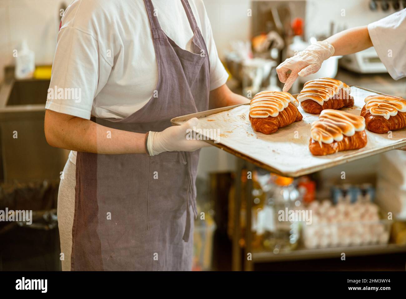 El confitero mantiene la bandeja con deliciosos cruasanes mientras su  compañero comprueba la producción en la panadería Fotografía de stock -  Alamy