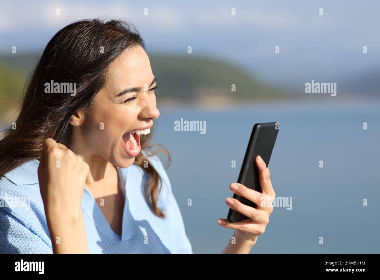 Mujer emocionado en un lago comprobando el teléfono inteligente de vacaciones Foto de stock