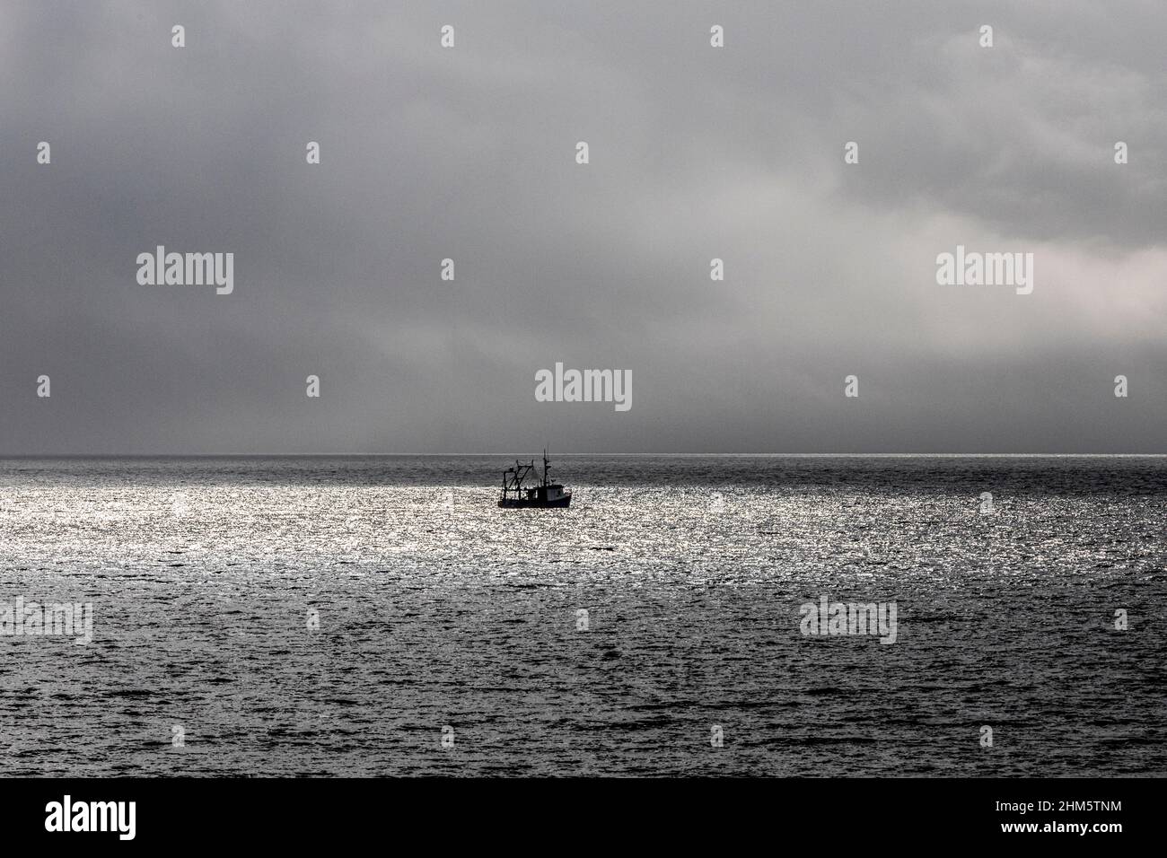 Un barco de pesca de bajura atrapado en un parche de luz solar en un día nublado en la bahía de Ardnross en la península de Kintyre, Argyll y Bute, Escocia Reino Unido Foto de stock