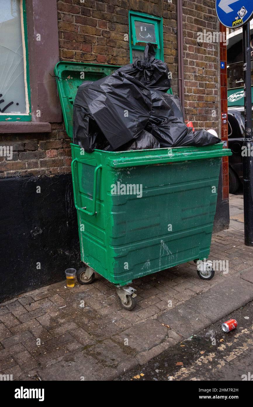 Un contenedor con bolsas de basura verdes desbordadas Foto de stock