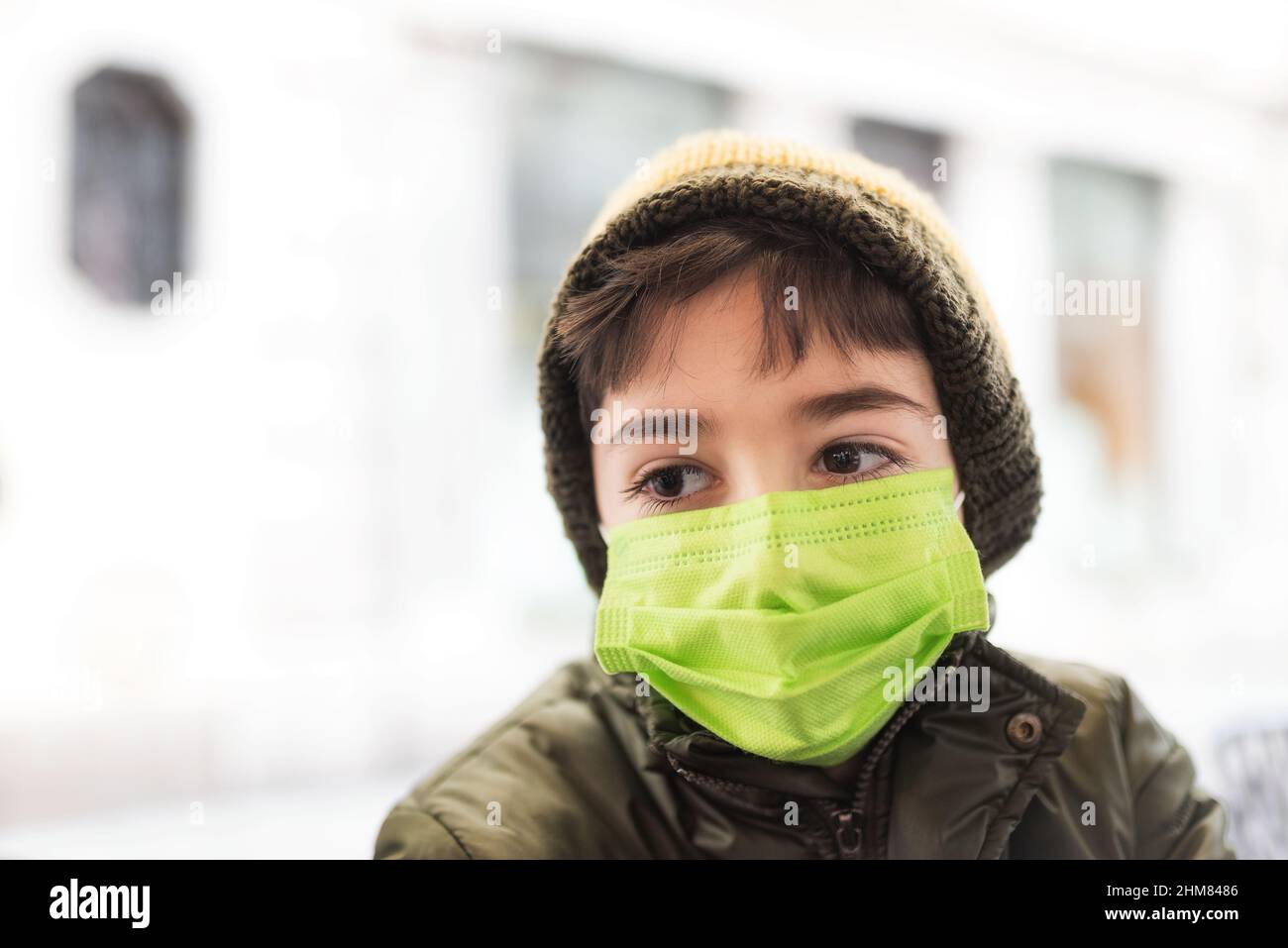Retrato de un niño de nueve años con una máscara quirúrgica verde. Concepto de protección Covid 19. Período OMICRON. Foto de stock