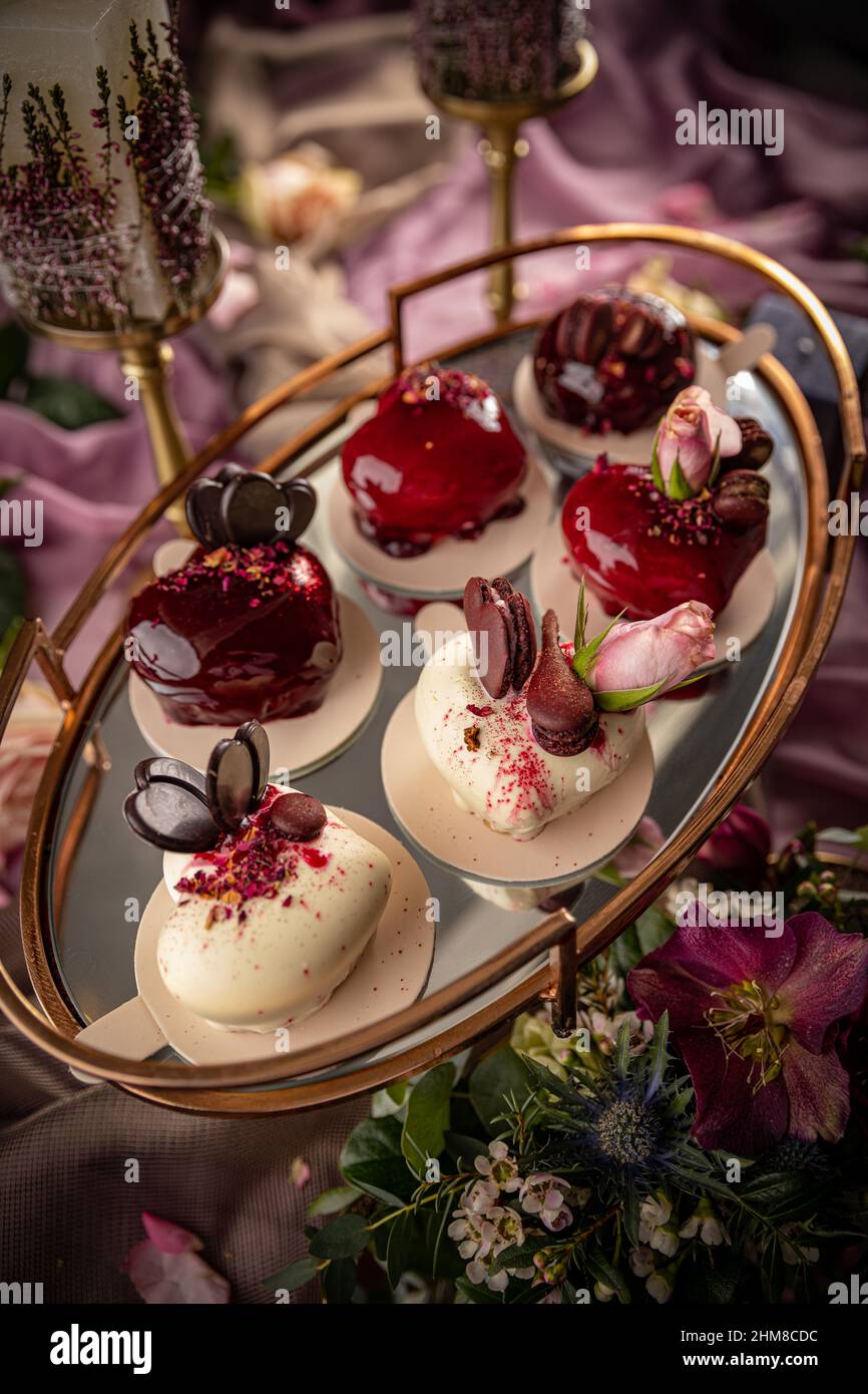 Pasteles de mousse modernos con espejos rojos y blancos en forma de corazón, decorados con rosas y chocolate. Día de San Valentín o pastel de boda todavía l Foto de stock