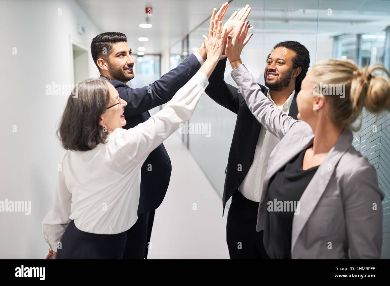 Feliz equipo de inicio de negocios celebrando el éxito con un alto cinco en el pasillo de la oficina Foto de stock
