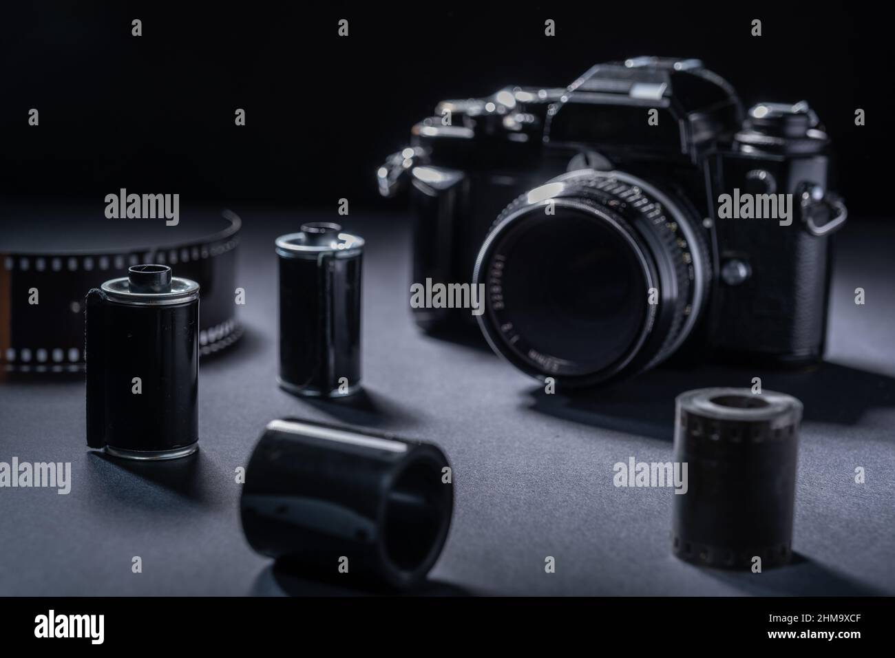 Fotografía de películas: Un cartucho de película metálica vintage y una cámara SLR 35mm sobre un fondo oscuro. Foto de stock