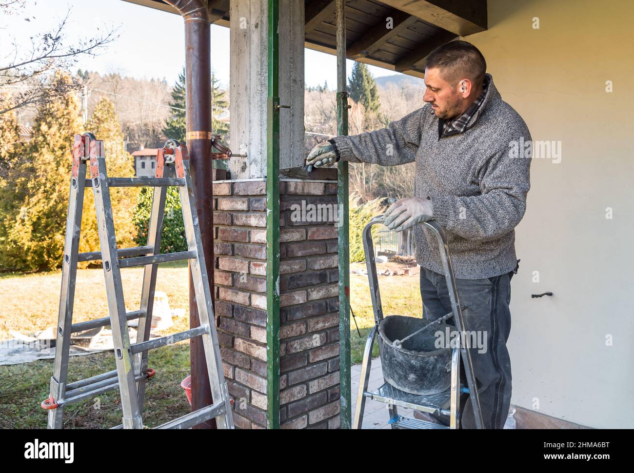 Trabajador de bricklayer instalando ladrillos en el pilar exterior de hormigón de la casa. El trabajador de la construcción que pone ladrillos. Foto de stock