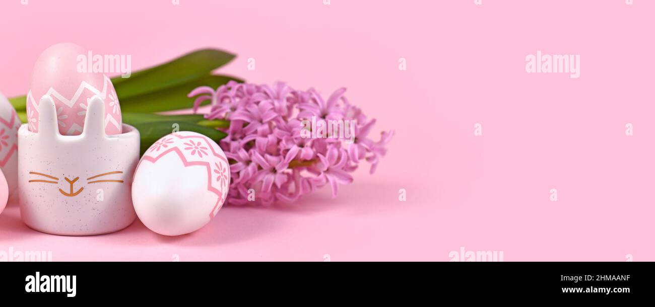 Pancarta de Pascua rosa con huevos y una taza de huevo en forma de conejito con flor de primavera de jacinto sobre fondo rosa Foto de stock