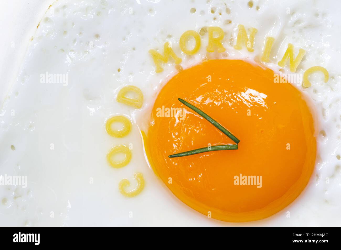 Huevo frito lado soleado en forma de reloj con letras de fideos para la buena mañana Foto de stock