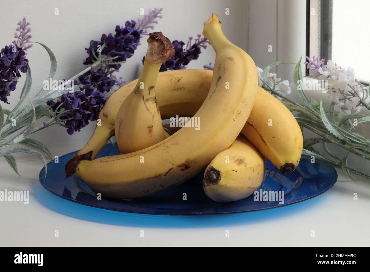 Todavía la vida con plátanos y flores artificiales. Está situado en un alféizar de la ventana. Primer plano. Foto de stock