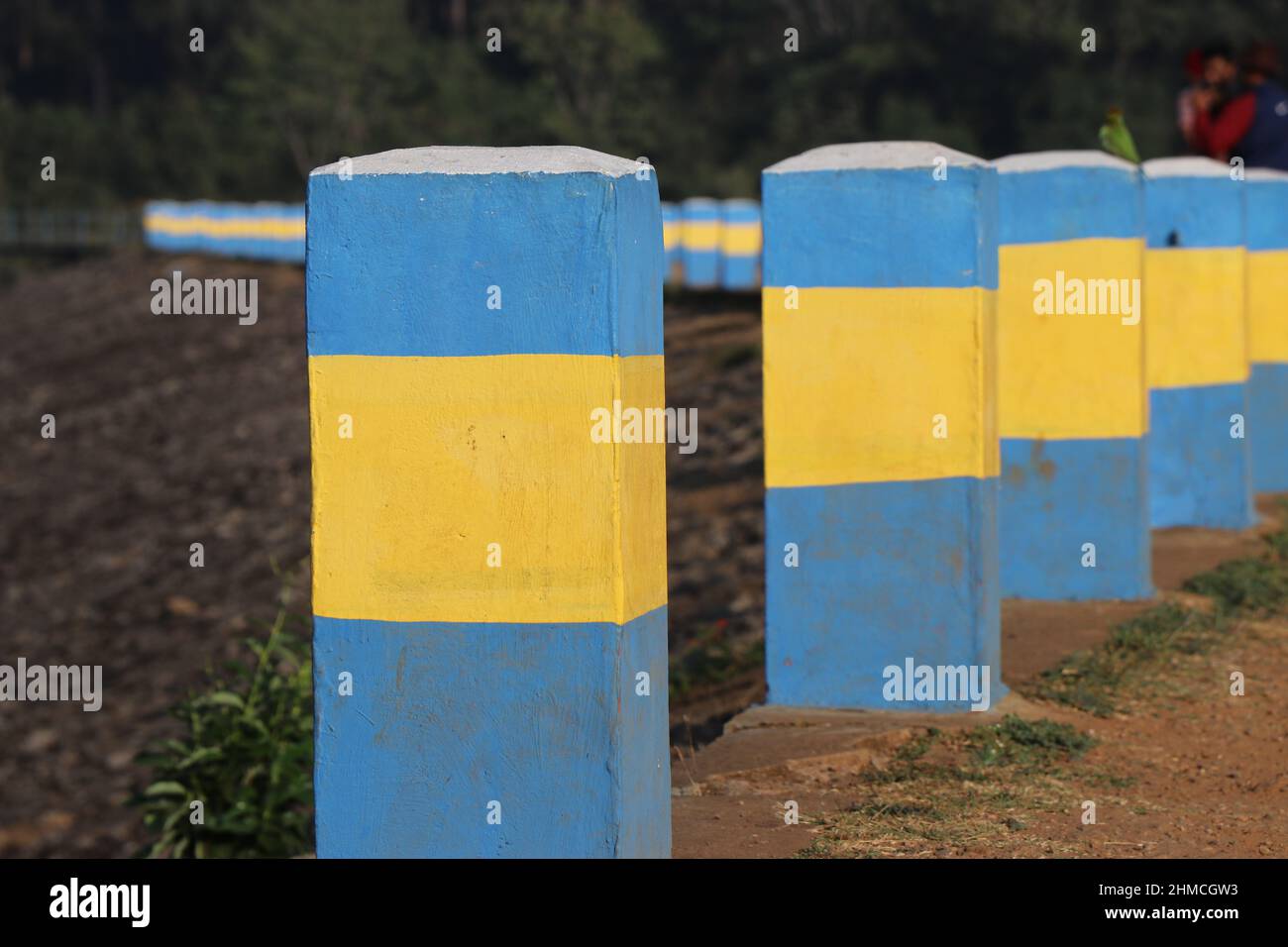 pivotes de hormigón pintados de azul y amarillo para delimitar las zonas de aparcamiento en el lado de la presa. Barreras de seguridad en la carretera Foto de stock