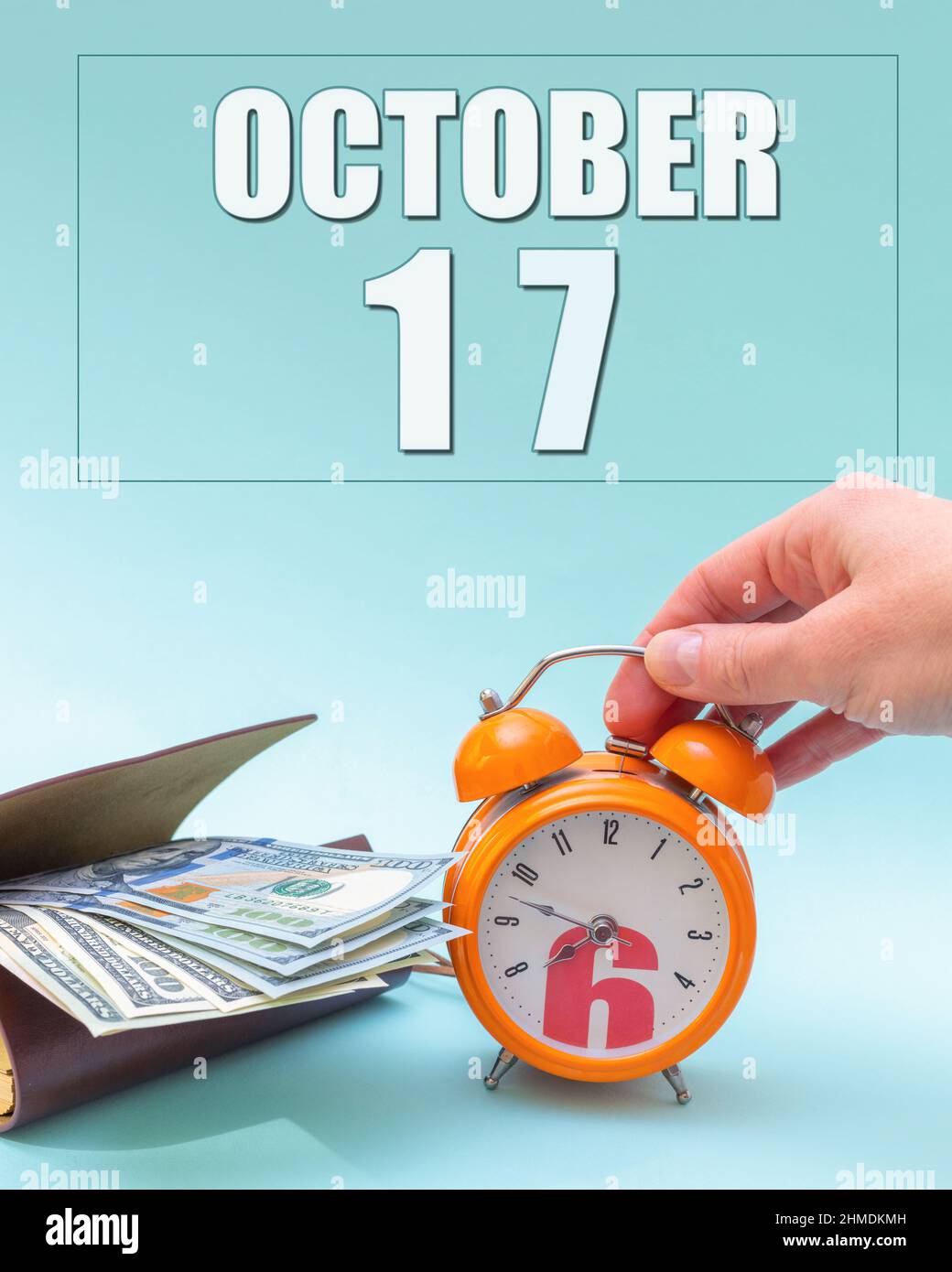 Octubre 17th. Mano sosteniendo un reloj de alarma naranja, una cartera con  efectivo y una fecha de calendario. Día 17 del mes. Planificación  empresarial. El tiempo es dinero. Tiempo de impuestos Fotografía