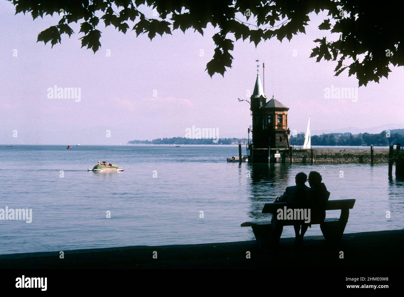 Pareja sentada en banco junto al puerto en 1981, Konstanz, Baden-Württemberg, Alemania Foto de stock